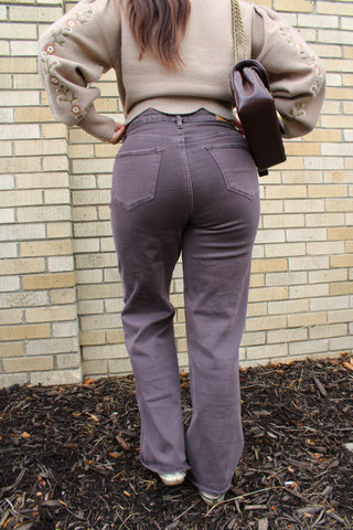 A person viewed from behind wearing Dear John Fiona high-waisted jeans, a beige sweater with floral embroidery on the sleeves, and carrying a dark brown shoulder bag available at Erin Rose boutique