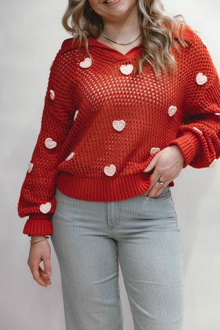 Person wearing a red sweater with heart patterns on a plain background available at Erin Rose Boutique