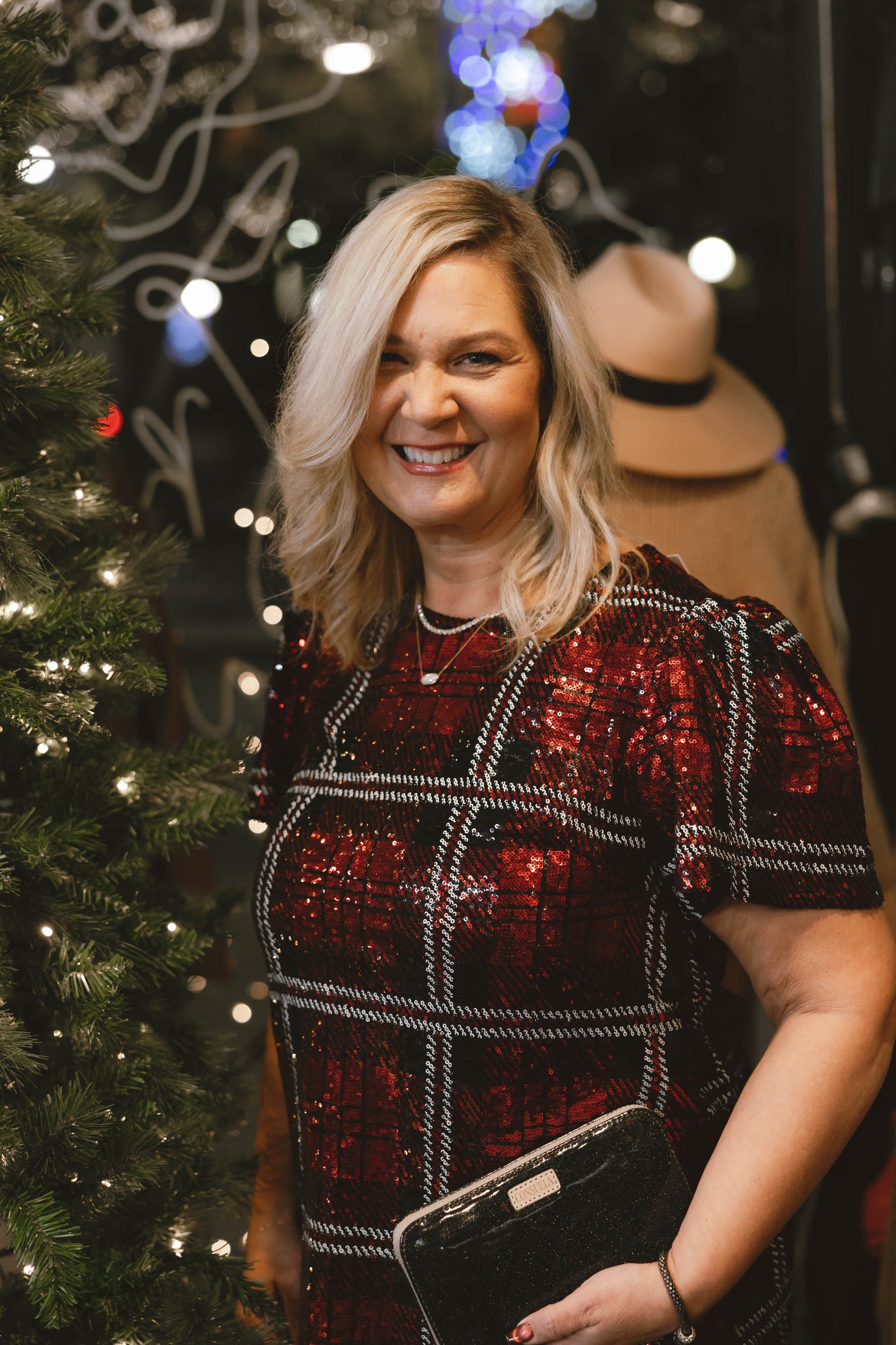 Woman in a red sequin plaid dress standing next to a Christmas tree with blurred background