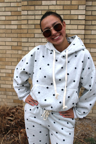 Person wearing a polka dot hoodie and pants in front of a brick wall.