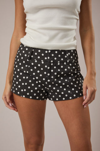 Model wearing black mid-rise shorts with white polka dots, styled with a fitted white tank top.