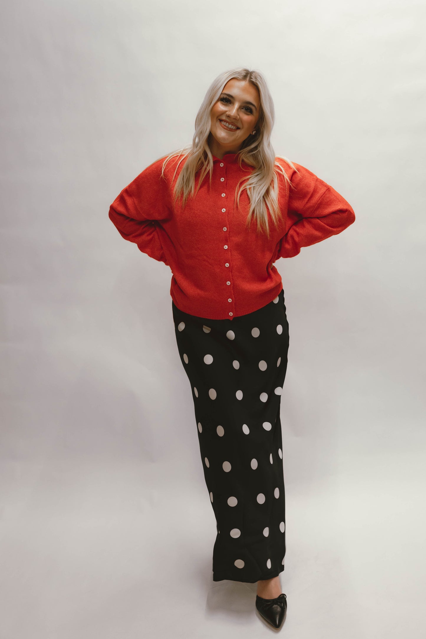 Person wearing a red cardigan and black polka dot silk skirt on a white background available at Erin Rose Boutique