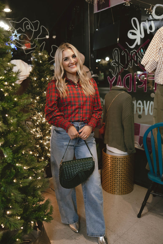 woman wearing red plaid smocked sleeve top with light wash wide leg jeans holding a green woven handbag at Erin Rose Boutique