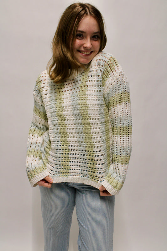 Woman wearing a sage green and cream striped open knit sweater styled with light blue striped pants.