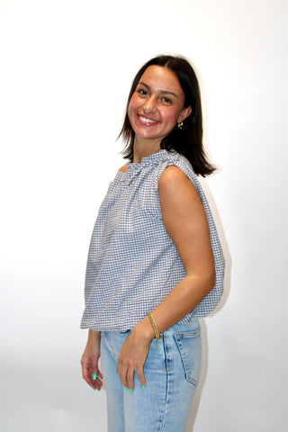 Woman wearing a gingham checkered sleeveless top with bubble hem and jeans against a white background
