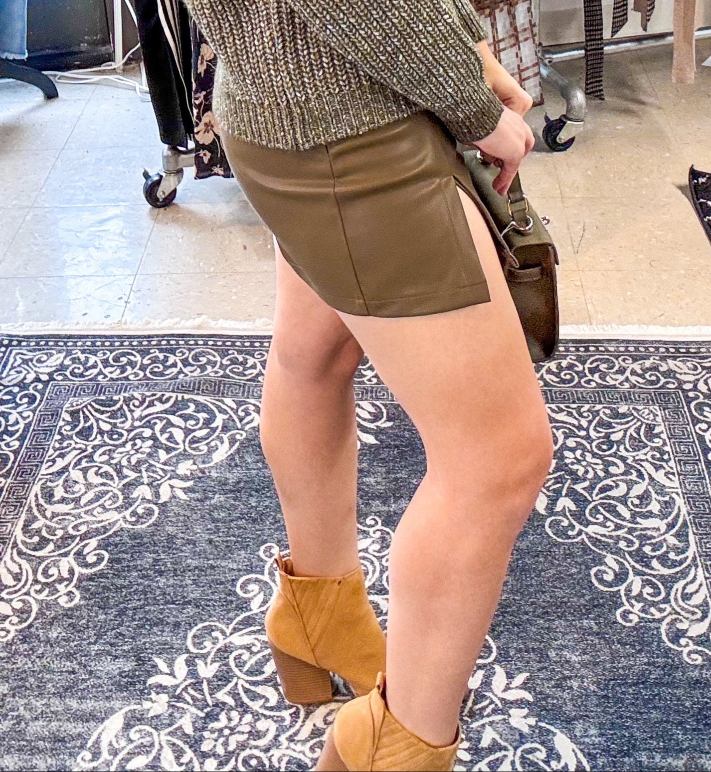 Woman in a clothing store wearing a green sweater and brown shorts.