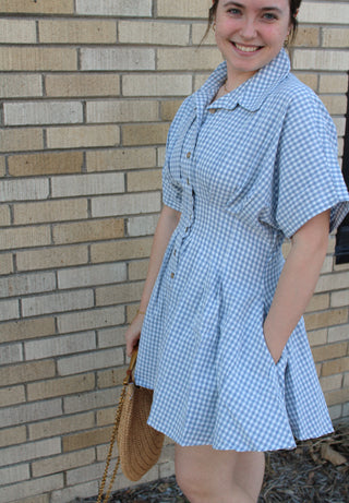 model wearing periwinkle blue gingham button front mini dress with flattering fit styled with woven handbag from Erin Rose Boutique