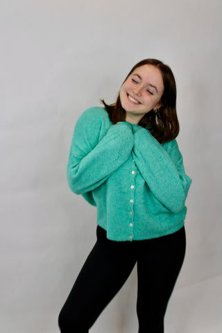 woman wearing a turquoise piper rolled collar button up cardigan sweater against a plain background