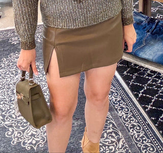 Woman in a clothing store wearing a patterned sweater and skirt, holding a handbag.