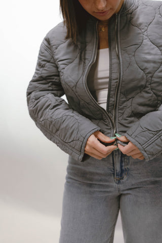 Woman wearing a blue quilted zip front jacket styled with light wash jeans.