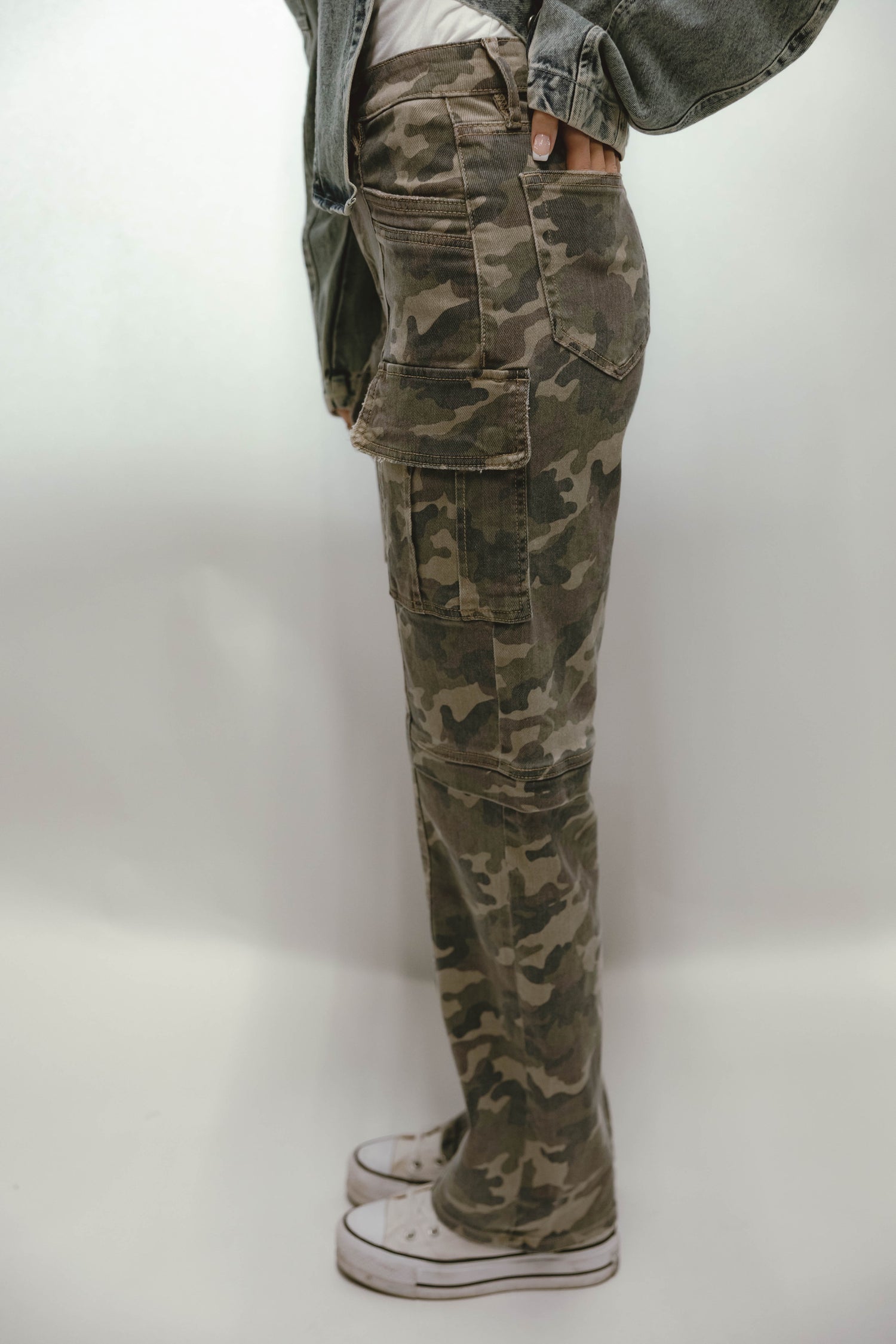 Woman wearing olive camo cargo straight leg pants styled with a denim jacket and white sneakers.