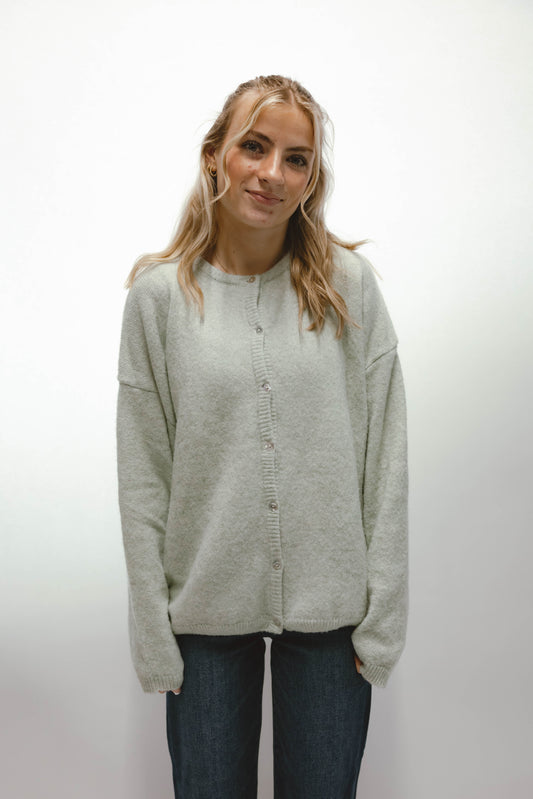Woman wearing a sage green button front knit cardigan styled with dark wash jeans.