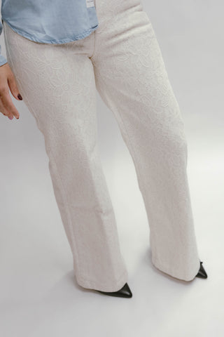 Woman wearing white floral lace wide leg pants styled with a light blue blouse and black pointed heels.
