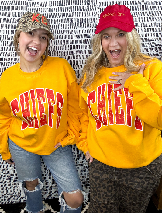 Two people wearing yellow sweatshirts with the word 'CHIEFS' printed in large red letters, smiling and posing for the camera.