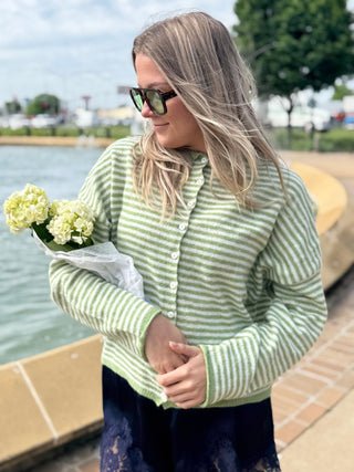 Woman wearing Abby Rose Mini Striped Piper Cardigan in matcha green and ivory stripes, lightweight knit button front sweater styled for a casual chic outfit.