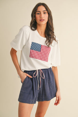 White knit top with balloon sleeves and American flag patch made of red gingham and blue stars