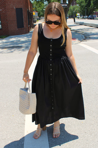 Model wearing a black sleeveless button front midi dress with neutral heels and a woven tote bag.