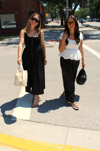 Model wearing a classic black sleeveless midi dress with front buttons and a woven tote bag.