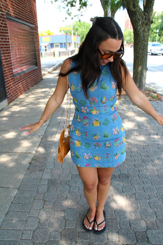 Woman wearing a blue floral embroidered shift dress with metallic sneakers and a woven purse.