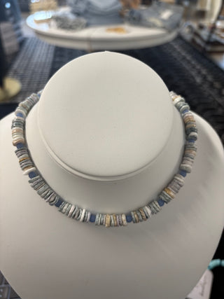 Blue and grey puka shell necklace with natural-toned disc beads displayed on a white bust stand, coastal-inspired jewelry 