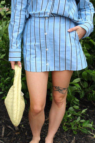Blue striped skort with button-front detail and relaxed fit styled with a matching striped blouse and woven handbag