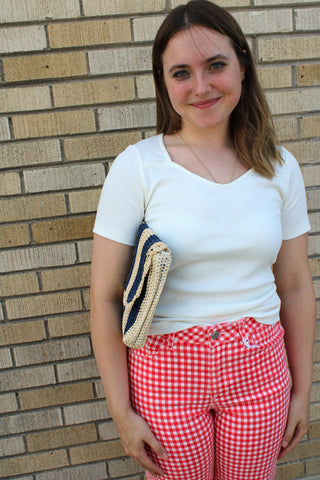 Woman wearing a cream ribbed square neck fitted top styled with red gingham pants and a woven clutch.