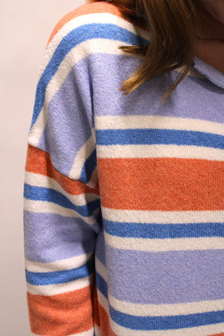 Close-up of a person wearing a fuzzy knit sweater with horizontal stripes in light lavender, blue, orange, and white.