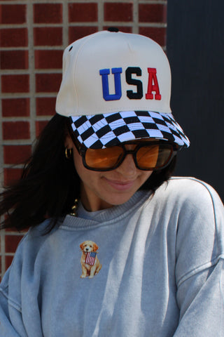 Woman wearing a cream trucker hat with USA embroidery and checkered brim detail.
