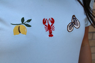 Light blue shirt with embroidered lemon, lobster, and oyster designs.
