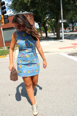Woman in a fitted blue mini dress decorated with colorful embroidered flowers and garden-inspired details.