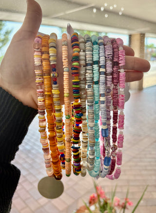Hand holding a variety of colorful puka shell necklaces with rainbow and pastel beads, perfect for layering and summer style from Erin Rose Boutique