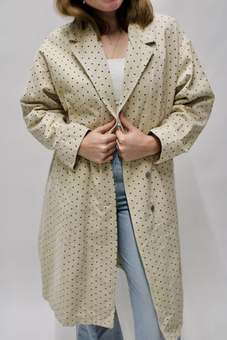 Woman wearing a cream long polka dot trench coat layered over a white top and striped pants.