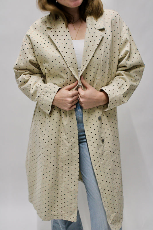 Woman wearing a cream long polka dot trench coat layered over a white top and striped pants.