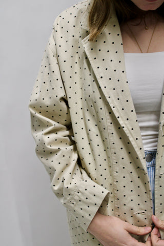 Close-up of a cream polka dot trench coat layered over a white tank and striped pants.