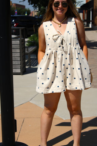Women's cream denim polka dot romper styled with a woven crossbody bag for a casual summer outfit.