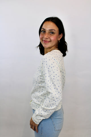 Woman wearing a cream button-front cardigan with delicate lilac micro floral print paired with light blue striped pants.