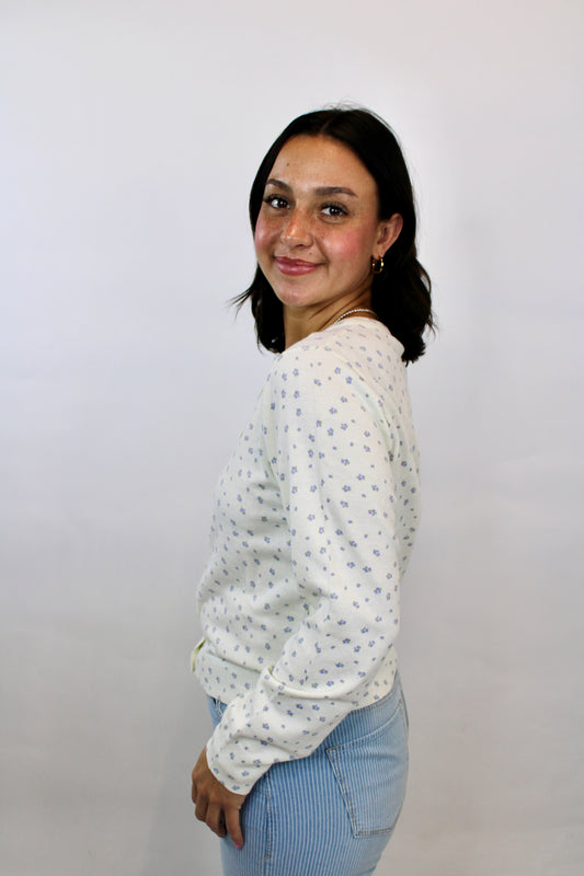 Woman wearing a cream button-front cardigan with delicate lilac micro floral print paired with light blue striped pants.
