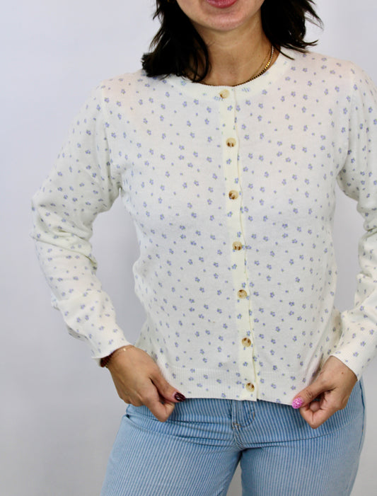 Woman wearing a cream button-front cardigan with small lilac floral print and light blue striped pants.