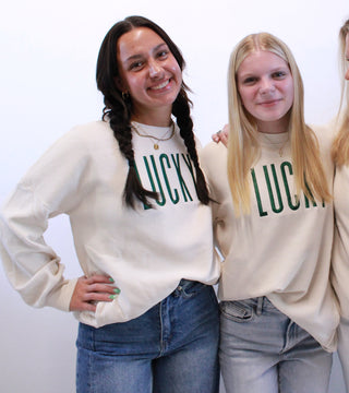 Three women wearing white sweatshirts with 'LUCCA' printed on them, standing against a plain background.