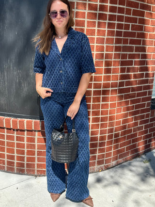 A woman wearing a matching navy blue patterned short-sleeve button-up shirt and wide-leg pants set, and holding a black textured handbag.