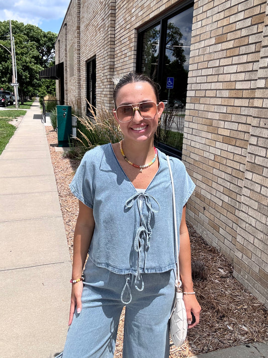 Woman wearing light wash denim tie-front top with cap sleeves outside Erin Rose Boutique