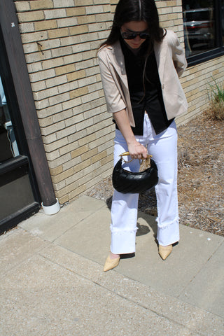 Woman wearing a beige cropped blazer layered over a black button-up top with white cropped denim.