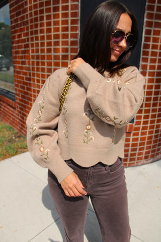 A woman wearing Flora Embroidered Knit Sweater in taupe with delicate floral embroidery and scalloped hem floral embroidery, paired with chocolate brown pants