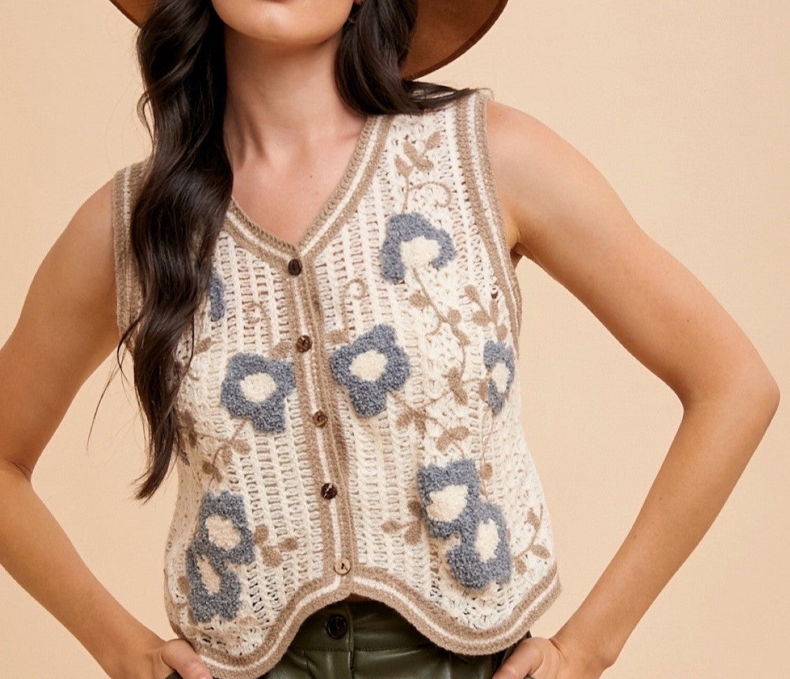 Woman wearing a cream crochet vest with blue and beige floral embroidery and button-up front – sleeveless boho knit layering top