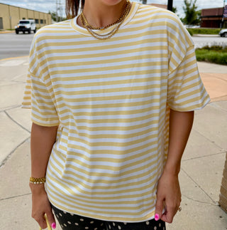Women's butter yellow and white striped oversized tee styled with polka dot pants, gold jewelry, and casual sandals.