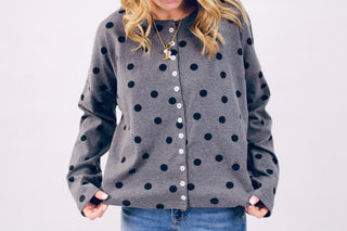 Person wearing a gray cardigan with black polka dots on a plain background