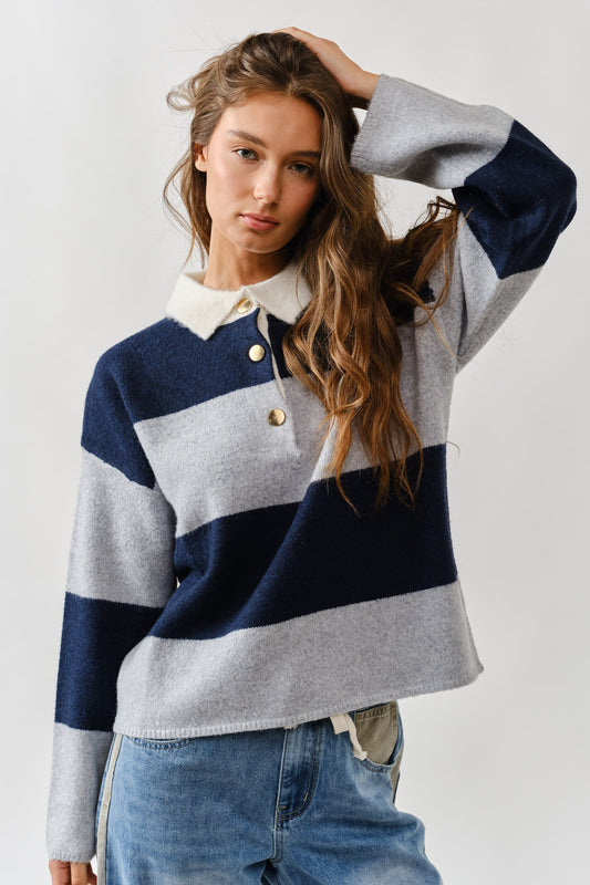Woman wearing a striped sweater with a white collar and blue jeans on a plain background