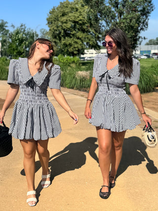Two women wearing the Honey Bee black and white gingham mini dress with an oversized collar, bow detail, and puff sleeves