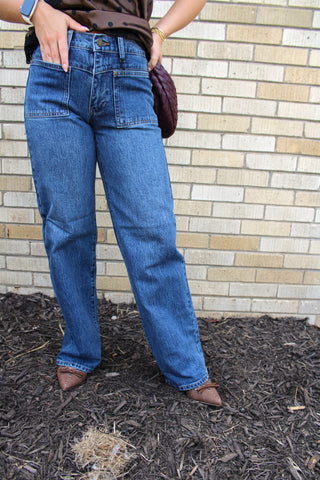 A person wearing JBD Square Patch Pocket Straight Jeans full front fit medium wash blue straight-leg denim jeans, brown pointed-toe heels, and holding a dark purple quilted clutch.