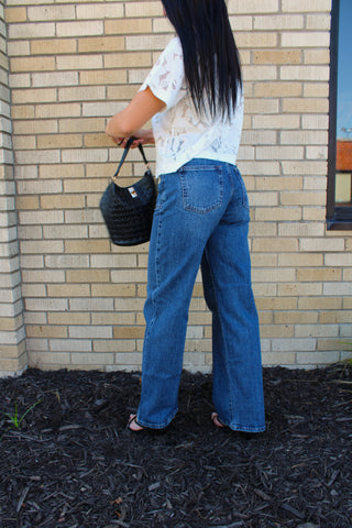 A woman from behind wearing jbd-square-patch-pocket-straight-jeans-full-length and a white lace top, holding a black woven handbag.
